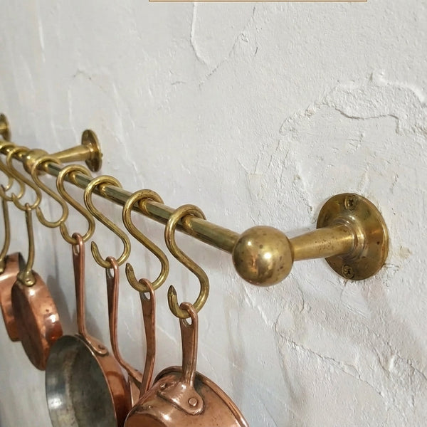 Unlacquered brass pot rail with brass hooks holding copper cookware, wall mounted kitchen pot hanger, farmhouse brass rail for hanging pots and pans.