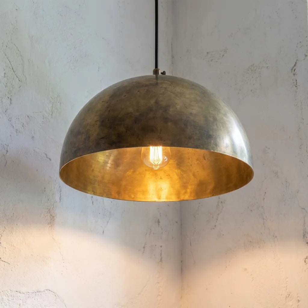 Brass pendant light hanging against a textured white wall
