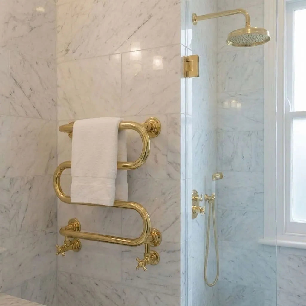 Luxury solid brass heated towel rail mounted in a marble bathroom beside a brass shower