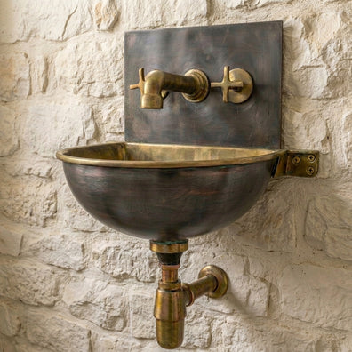 Brass wall-mounted sink with faucet against a stone wall
