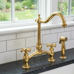 Gold kitchen faucet set on a black marble countertop with a window in the background.