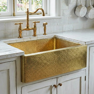 Hammered brass farmhouse apron-front kitchen sink with bridge faucet on white tile countertop