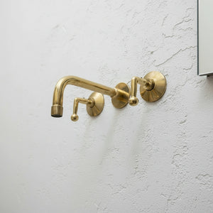 Brass wall-mounted faucet on a light gray wall