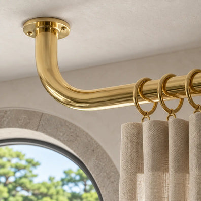 Close-up of round ceiling flange and curved return on an unlacquered brass curtain rod