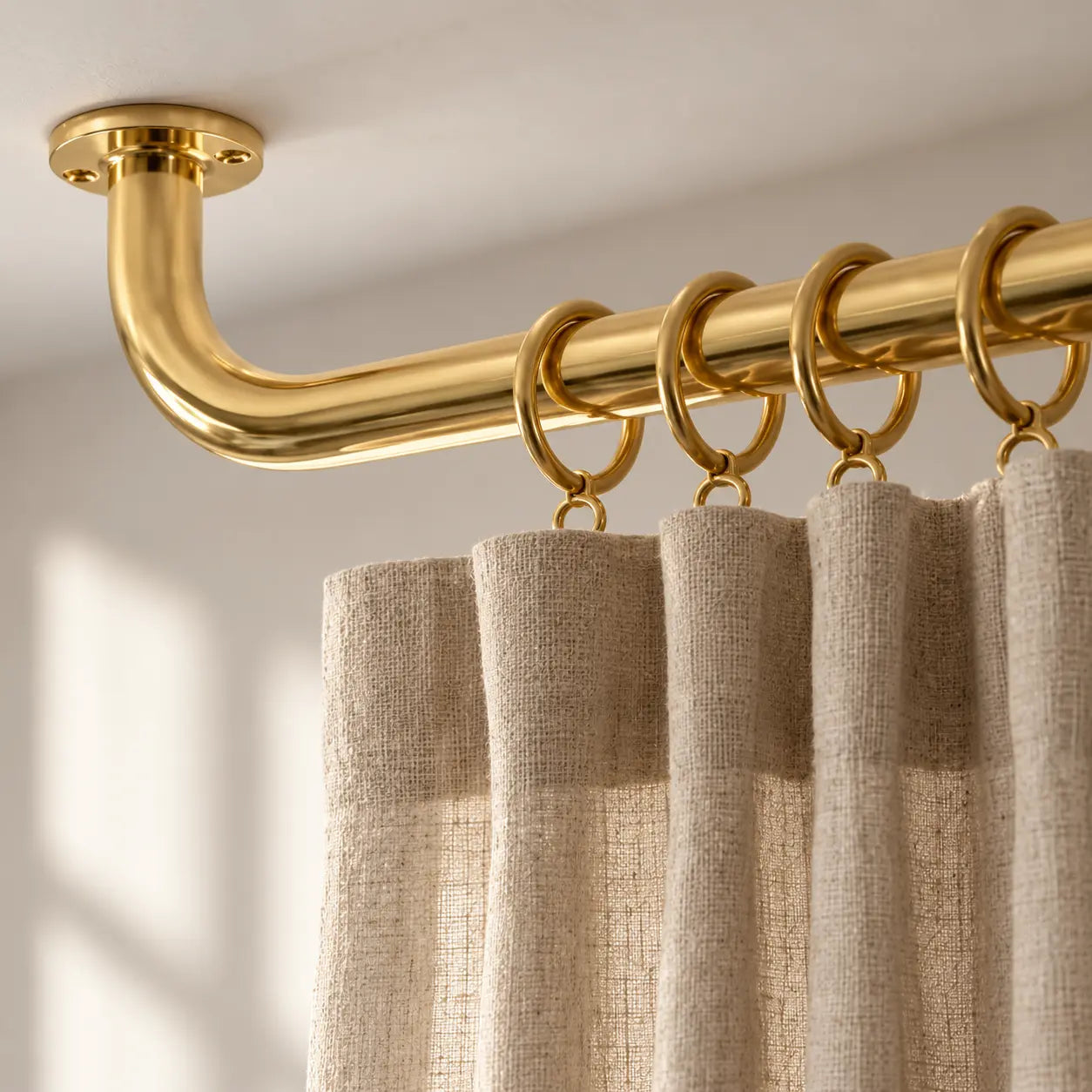 Close-up of matching brass curtain rings and linen drapes on a ceiling-mounted rod