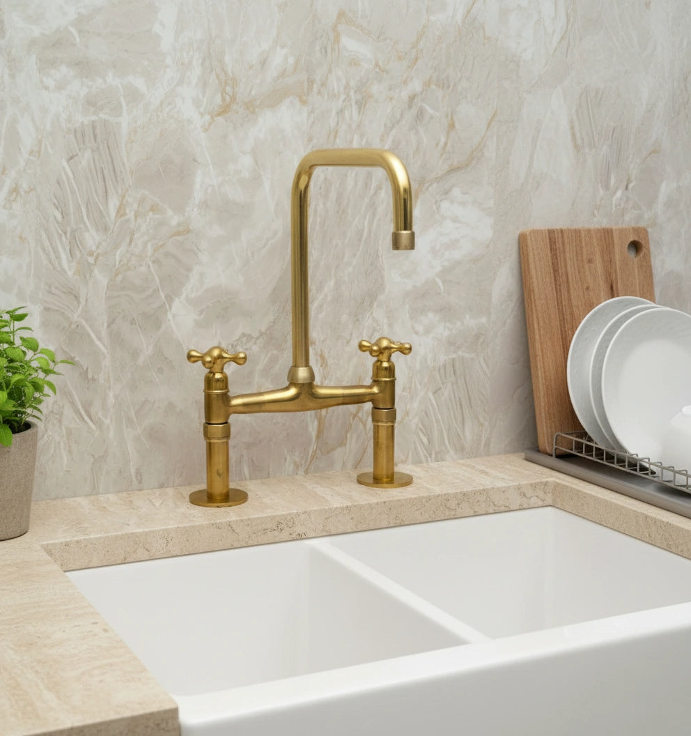 Gold kitchen faucet over a white sink with a neutral tiled wall background
