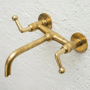 Brass wall-mounted faucet on a textured white background