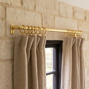 Extra-long unlacquered brass curtain rod with matching rings above a wide window