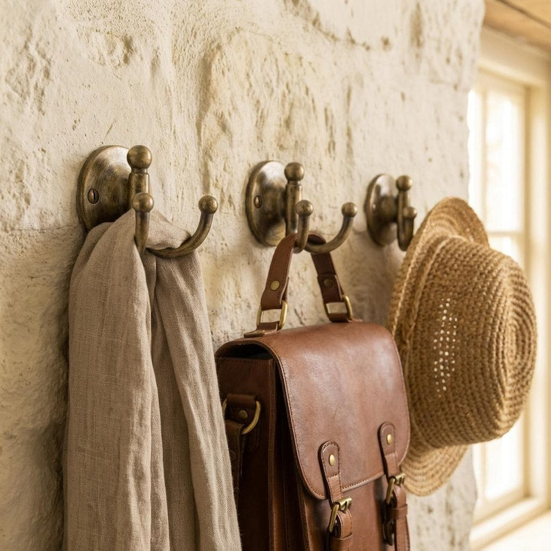 Three wall hooks with a coat, bag, and hat on a textured stone wall.