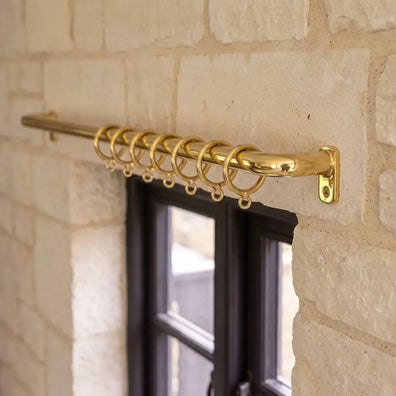 Large solid brass curtain rod with matching rings and wall brackets, close-up