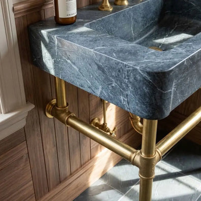 Unlacquered brass console sink legs beneath a dark gray marble basin, detailed view