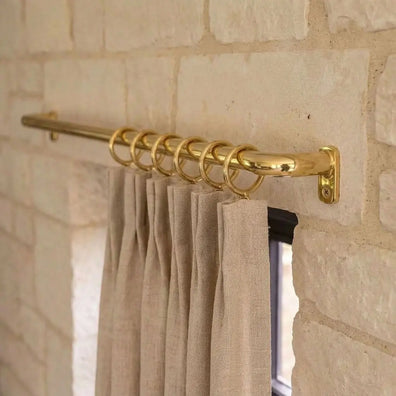 Unlacquered brass curtain rail with rings and linen drapes installed above a window