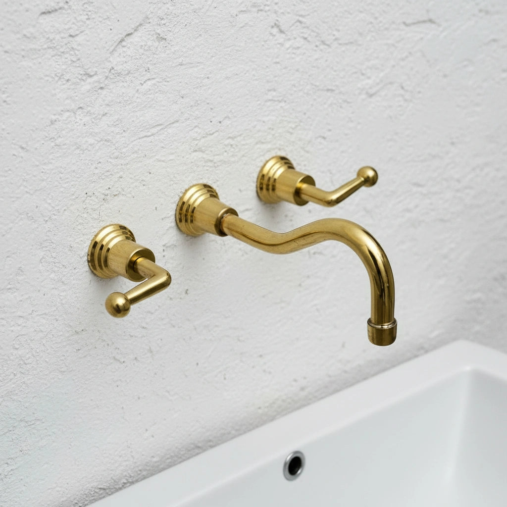 Gold faucet and handles on a white sink against a light gray wall