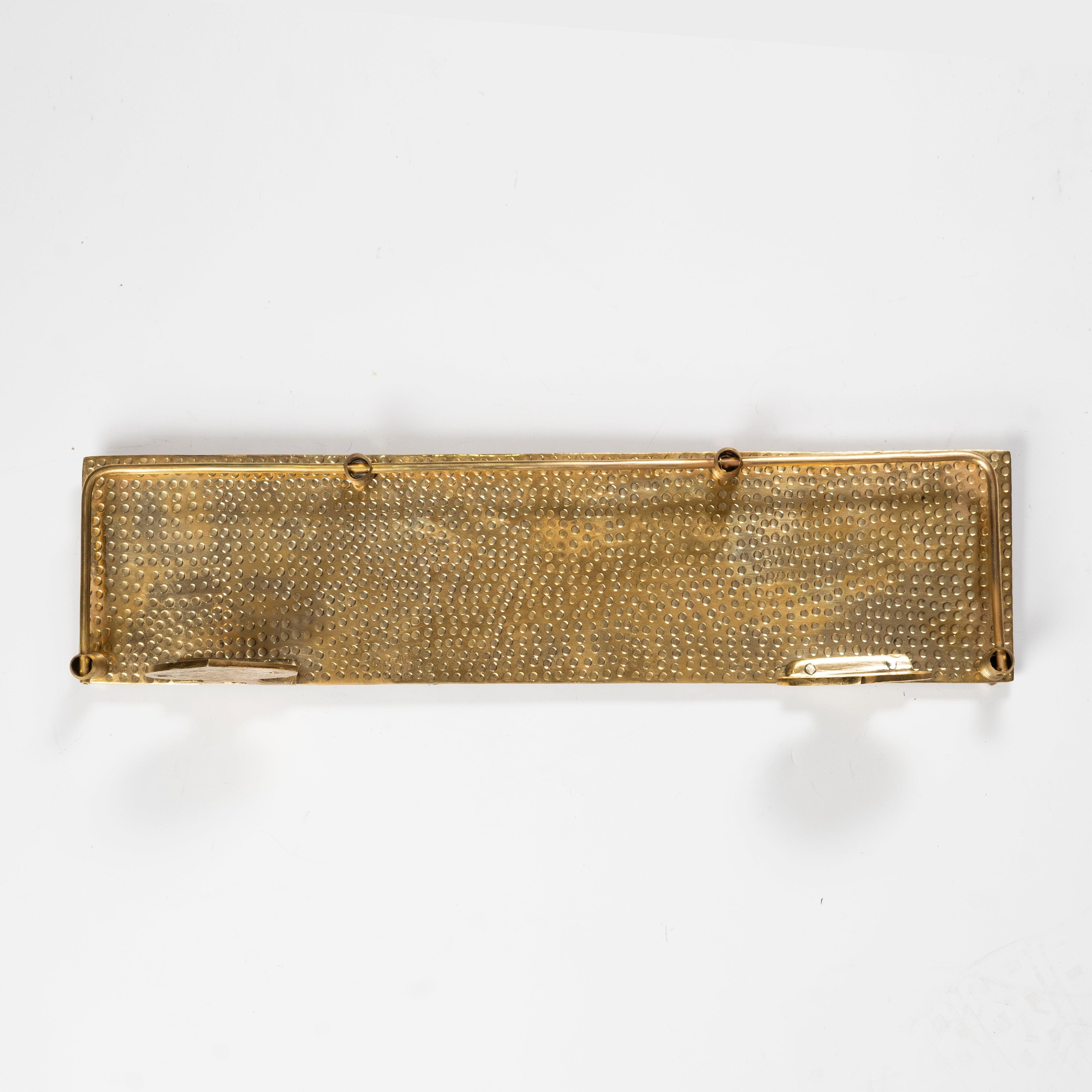 Underside view of a handmade hammered brass floating wall shelf with guard rail