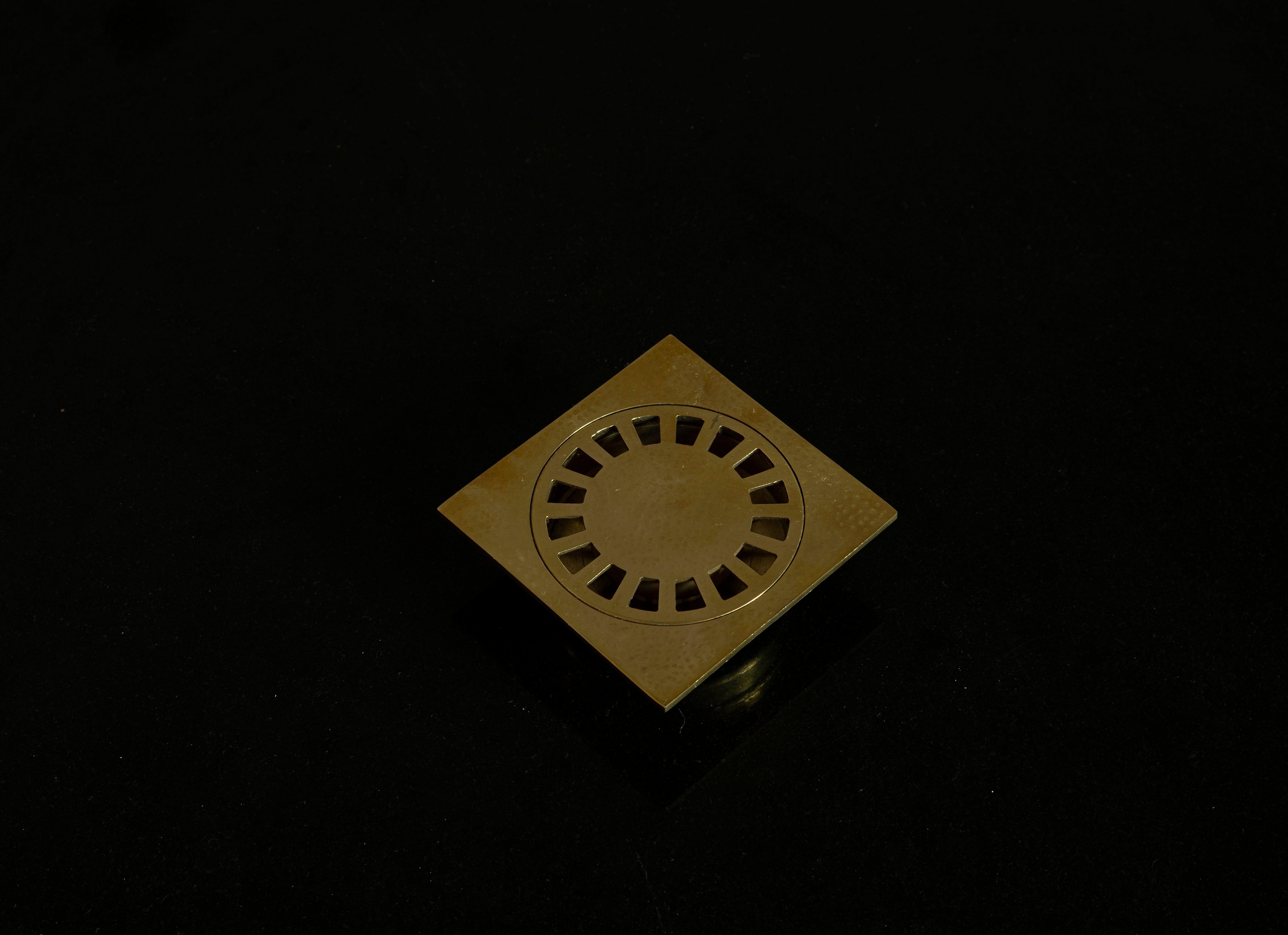 Hammered brass square shower drain with removable round grate on a black background