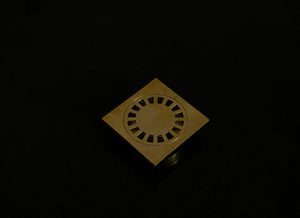 Hammered brass square shower drain with removable round grate on a black background