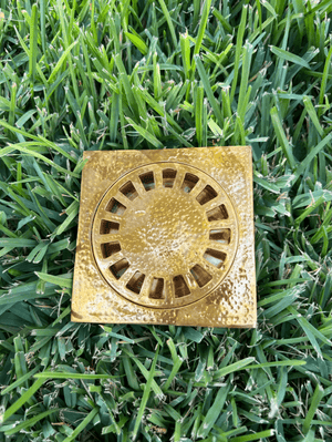 Hammered brass square shower drain with removable cover displayed on grass