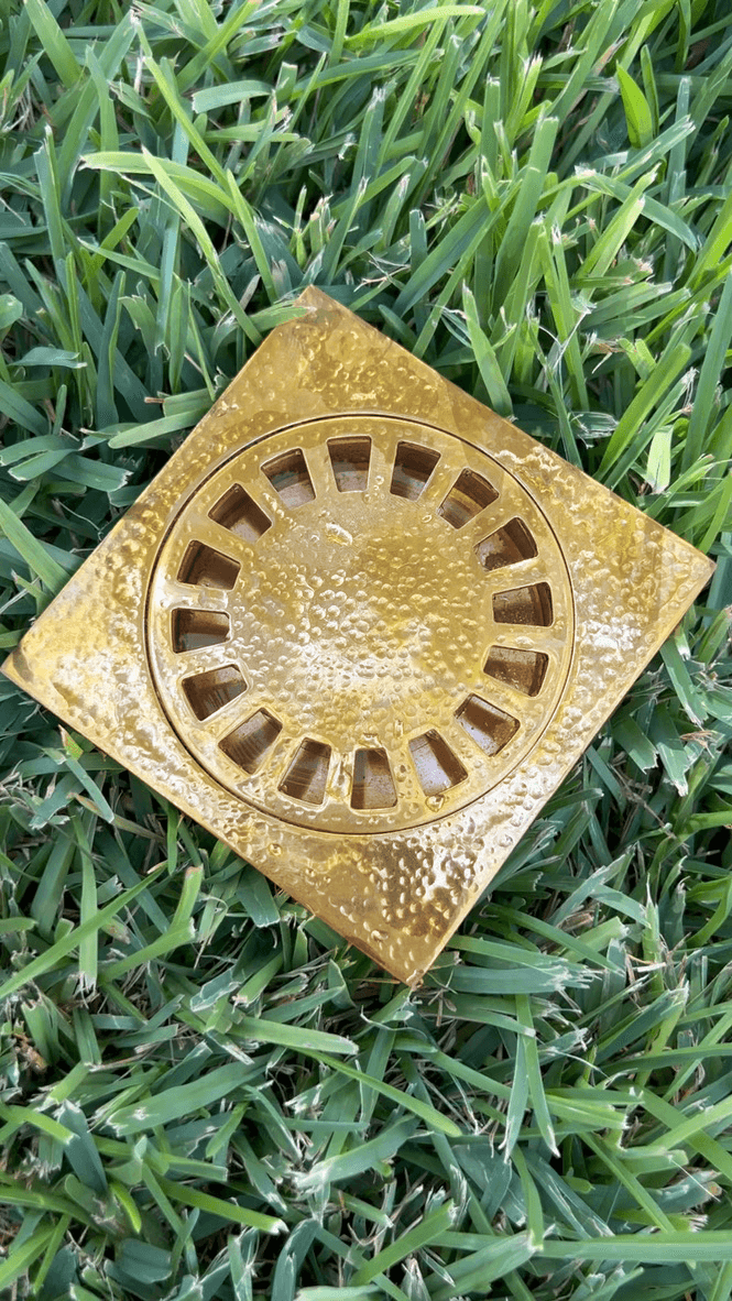 Hammered unlacquered brass square floor drain photographed on green grass