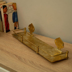 Hammered unlacquered brass wall shelf with guard rail displayed on a wooden table