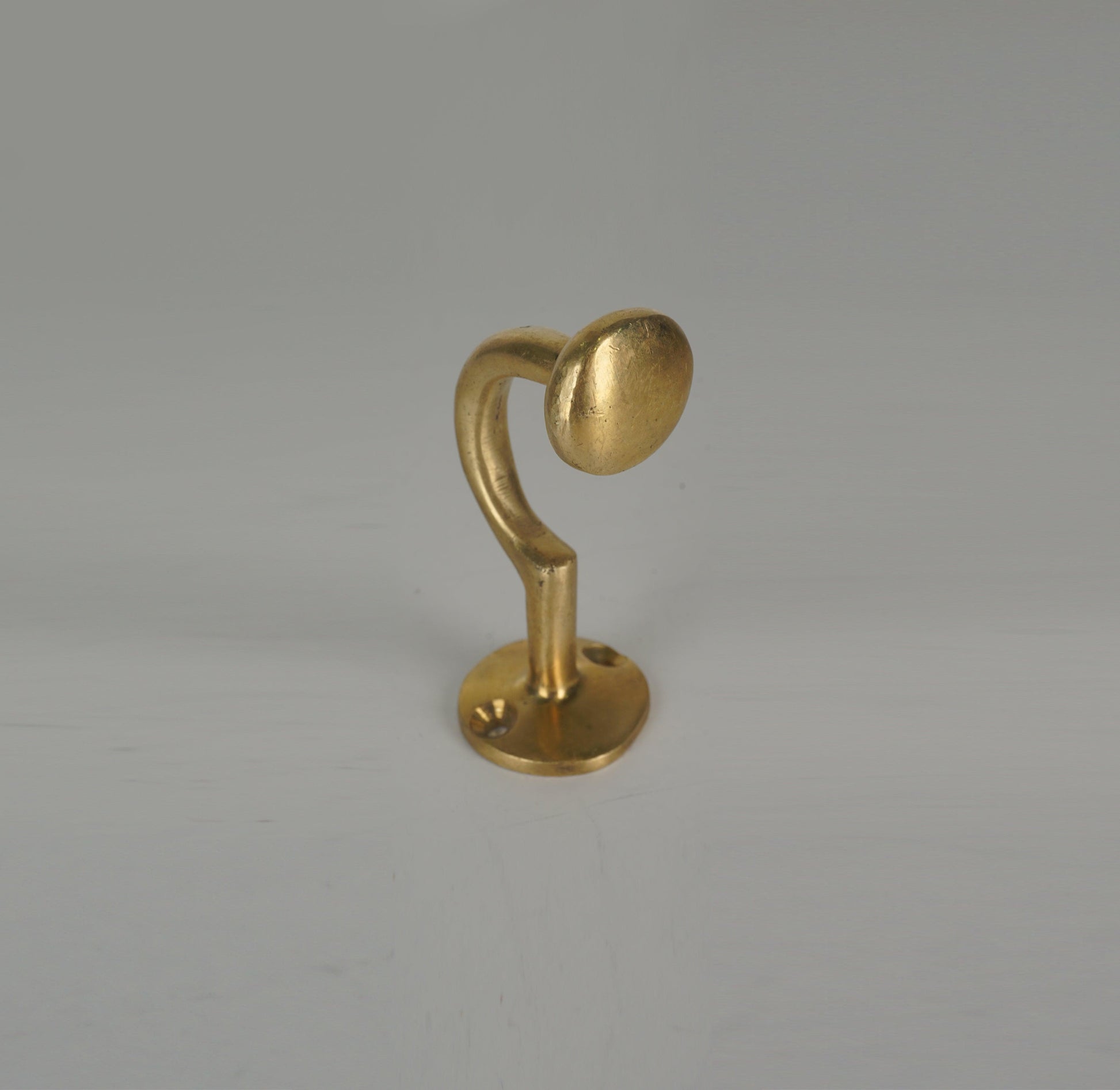 Front angled view of a handmade brass coat hook with rounded end and circular base