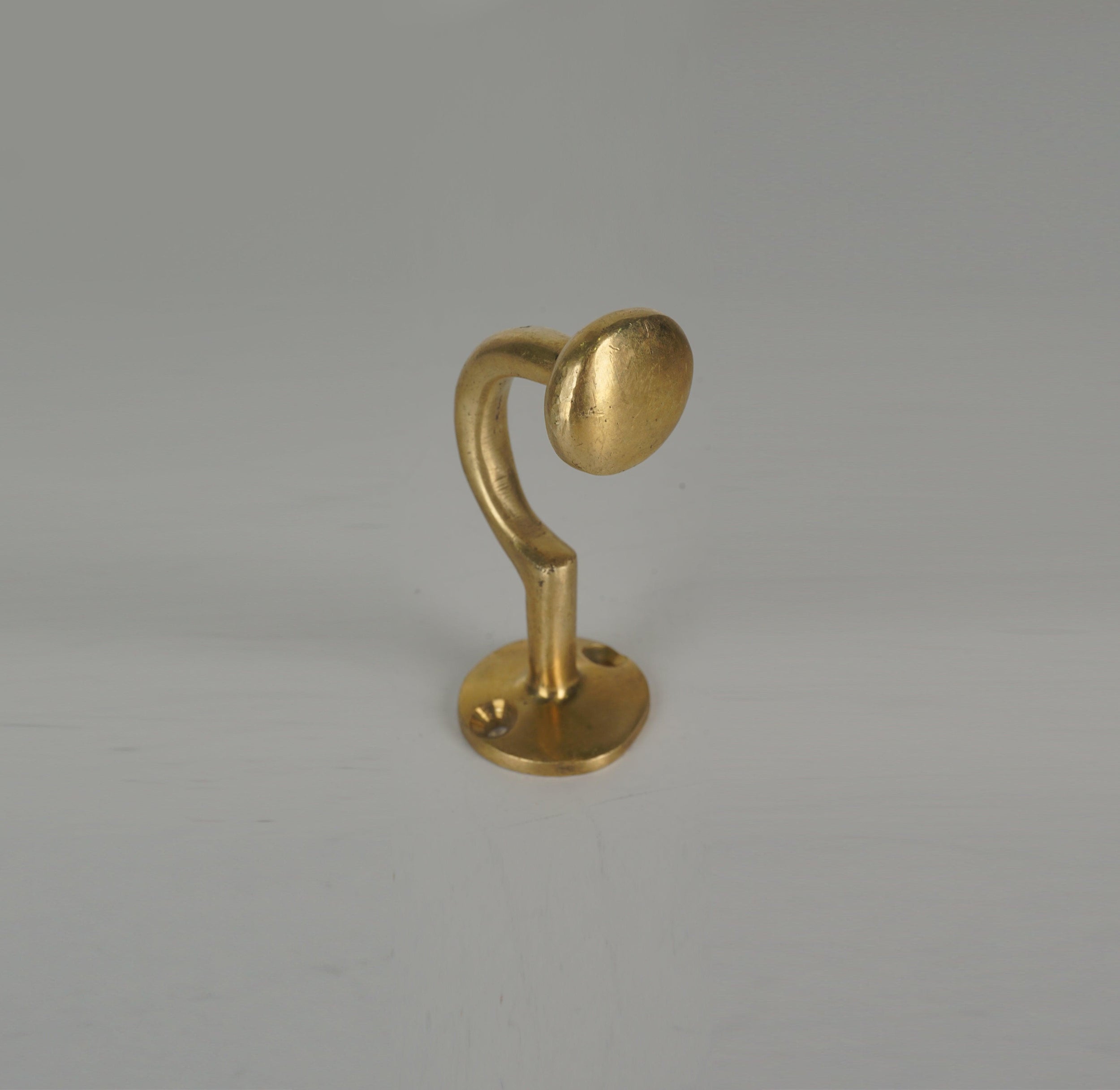 Front angled view of a handmade brass coat hook with rounded end and circular base