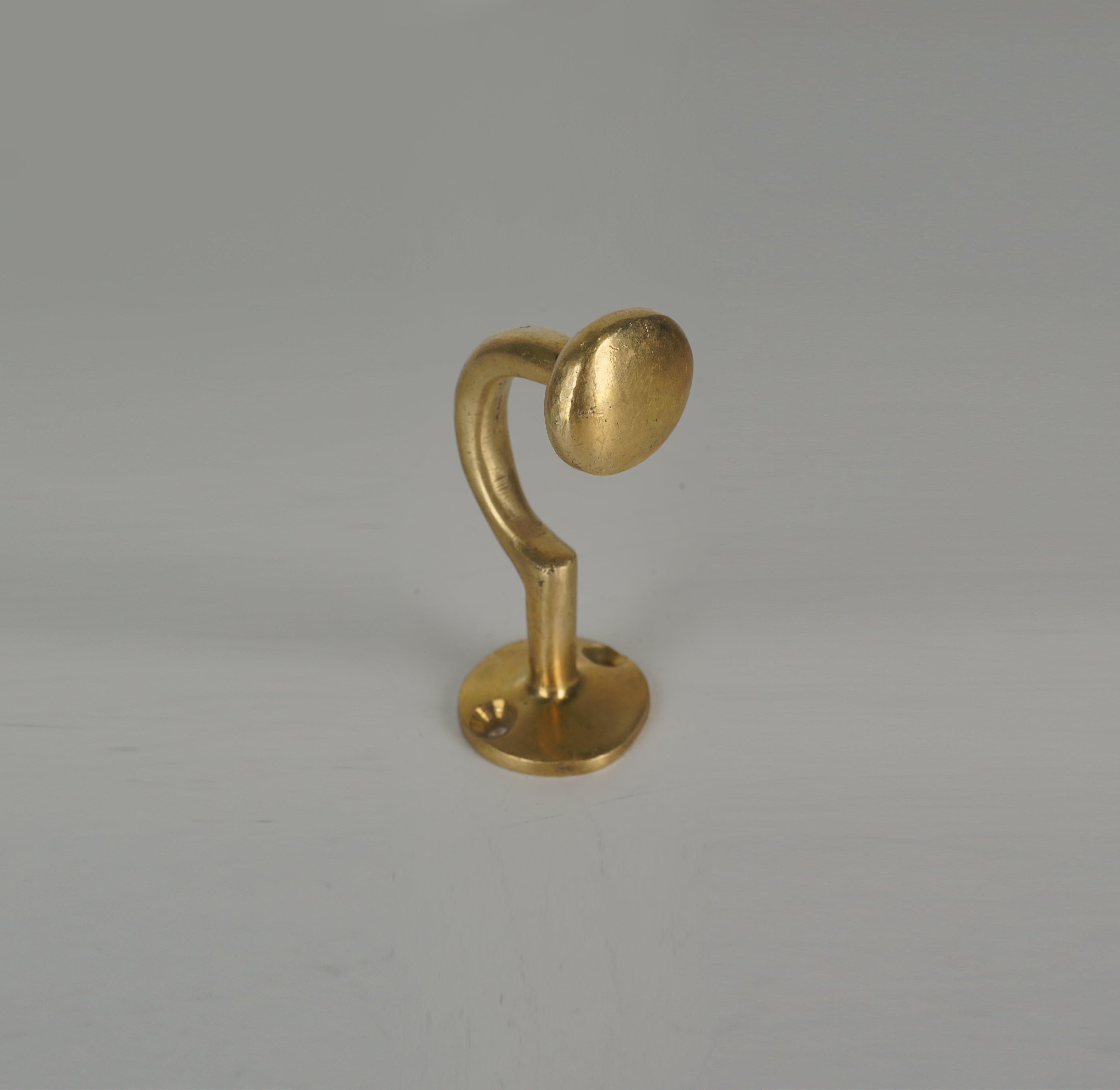 Front angled view of a handmade brass coat hook with rounded end and circular base