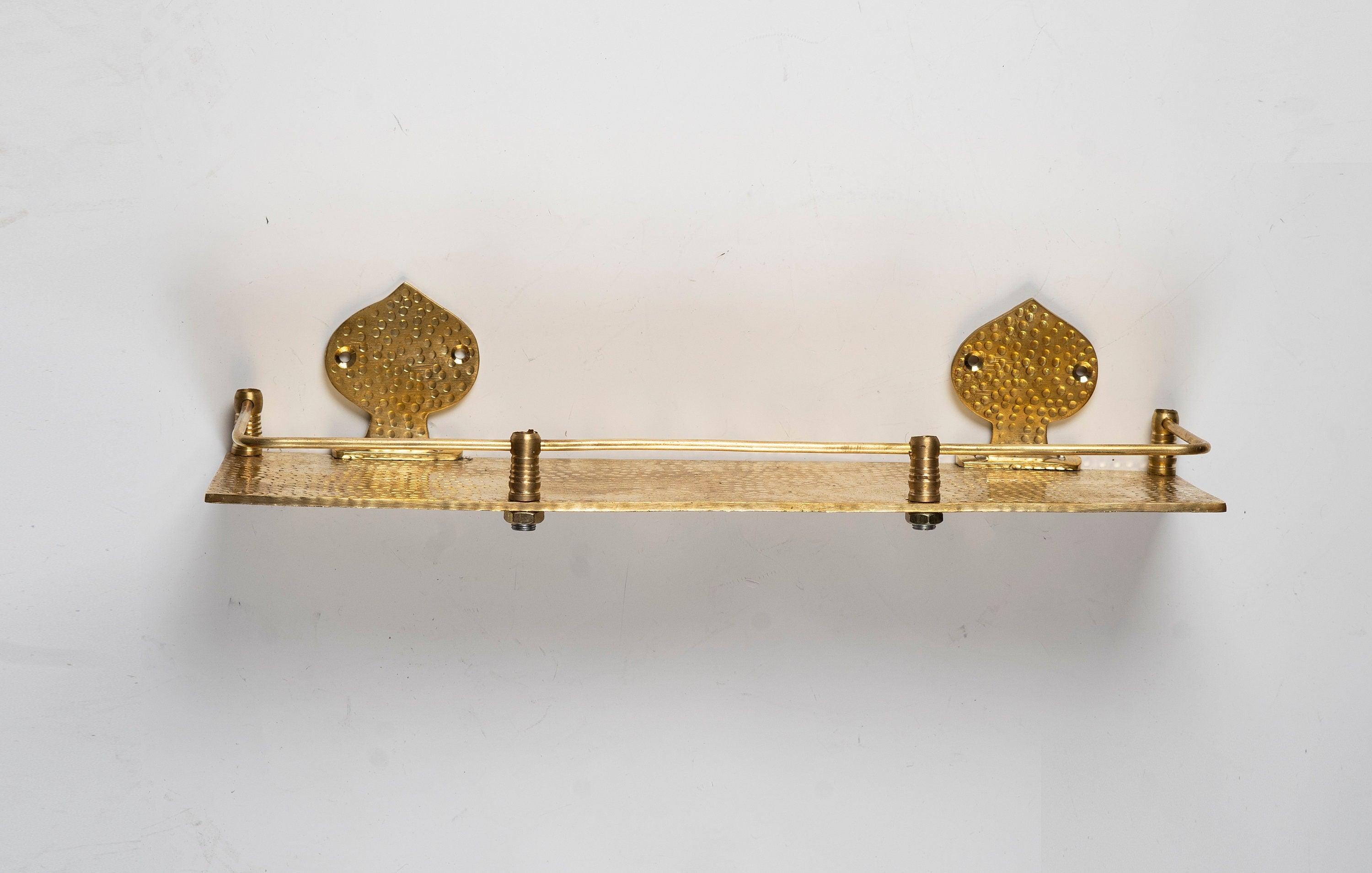 Front view of a handmade hammered brass floating wall shelf with decorative backplates and guard rail