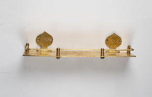 Front view of a handmade hammered brass floating wall shelf with decorative backplates and guard rail