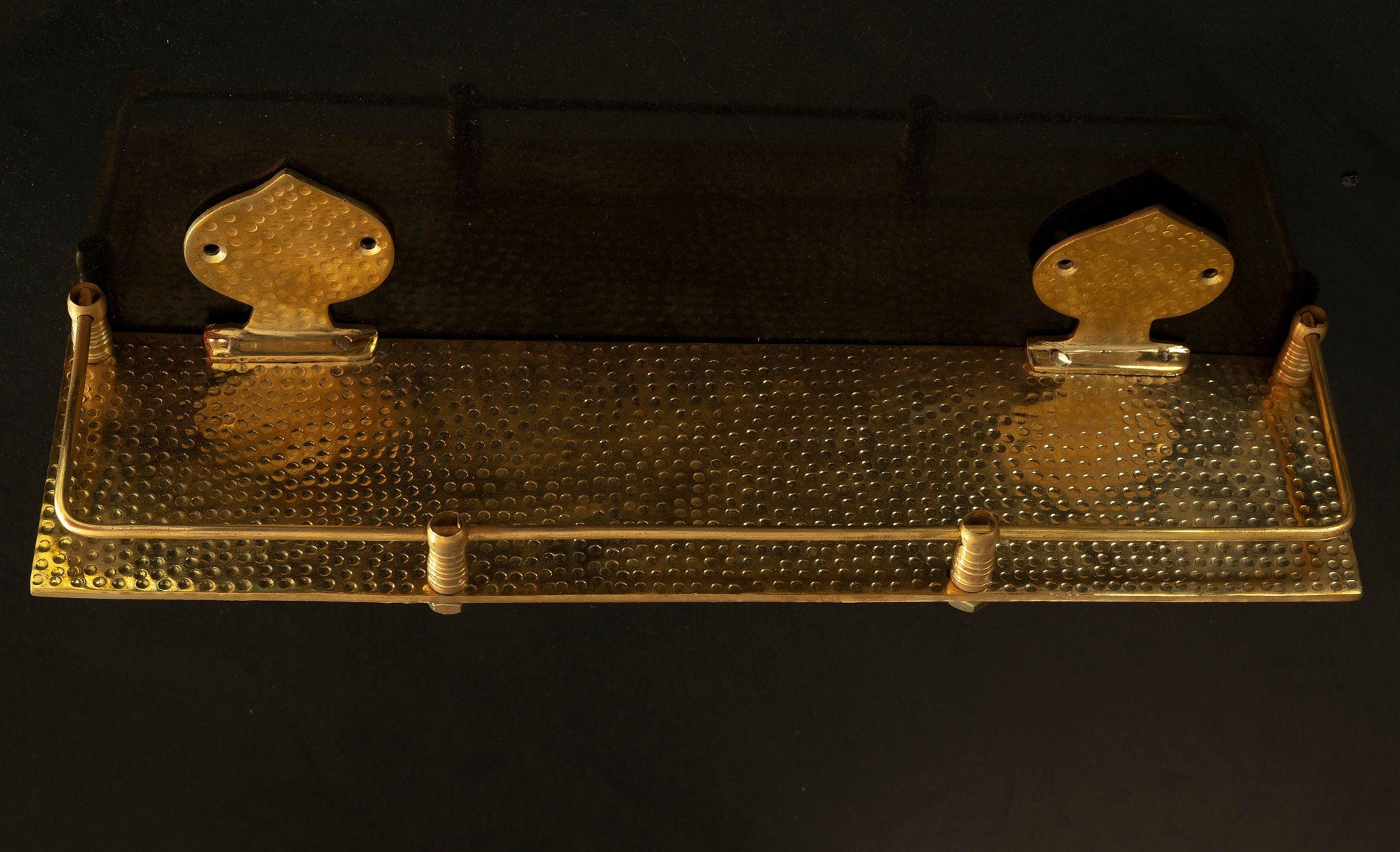 Solid brass hammered floating bathroom shelf with front rail on a black background