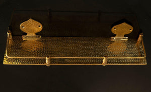 Solid brass hammered floating bathroom shelf with front rail on a black background
