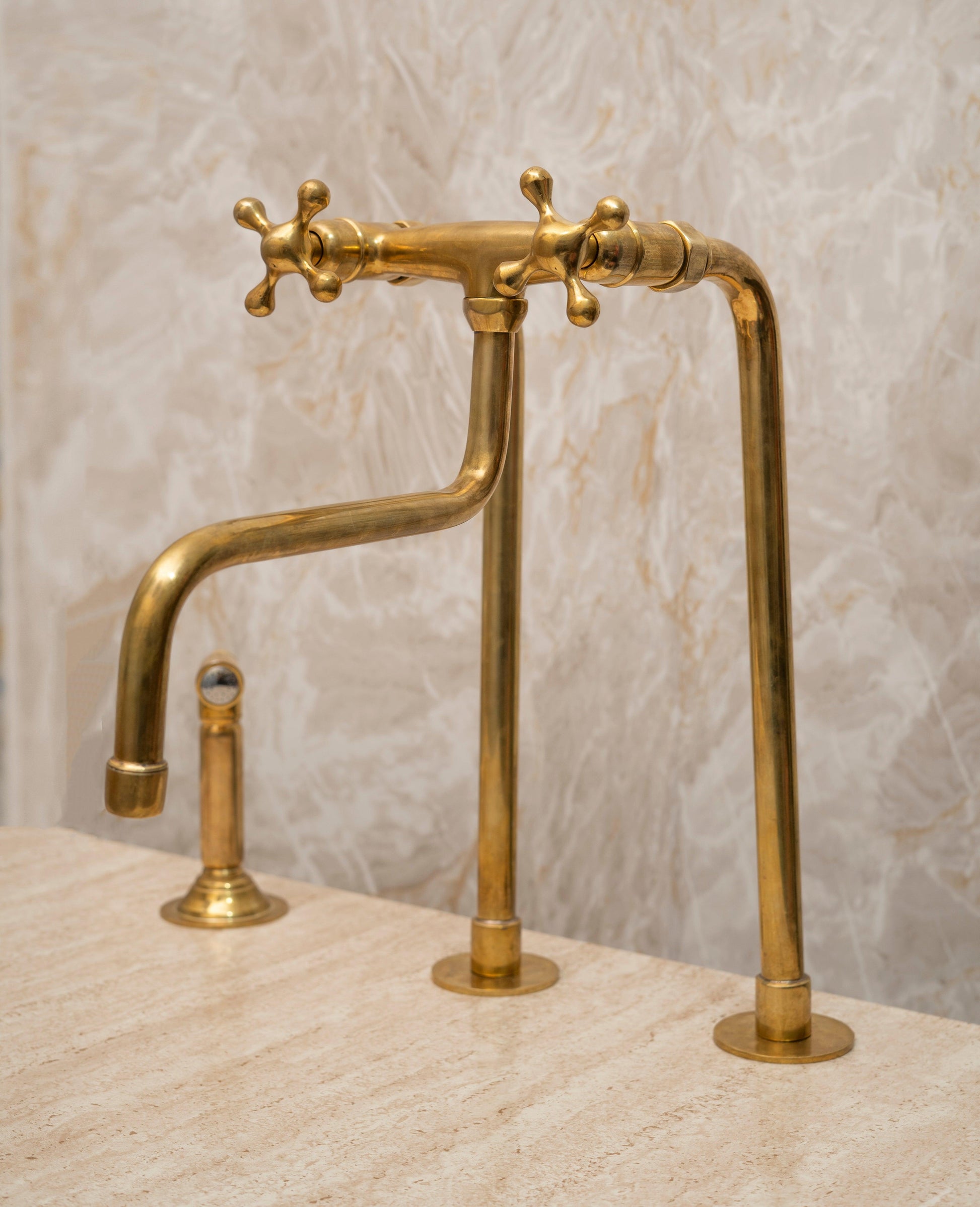 Angled view of a tall unlacquered brass bridge farmhouse faucet with side sprayer