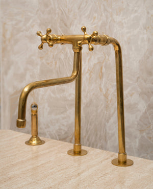 Angled view of a tall unlacquered brass bridge farmhouse faucet with side sprayer