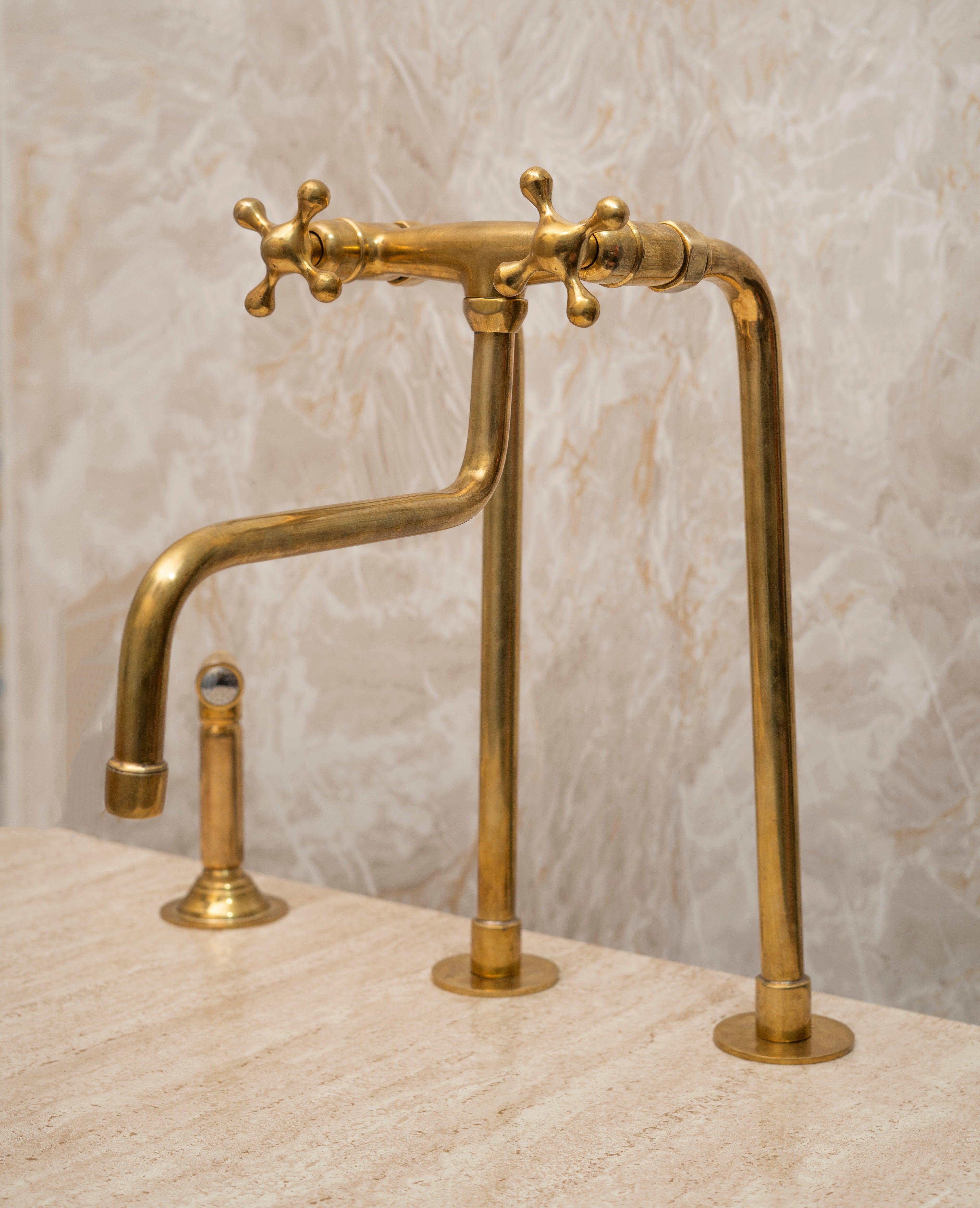 Angled view of a tall unlacquered brass bridge farmhouse faucet with side sprayer