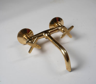 Angled view of an unlacquered brass bathroom tub filler faucet with cross handles