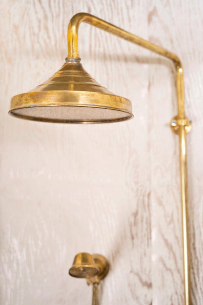 Close-up of an unlacquered brass round rain shower head on an exposed riser