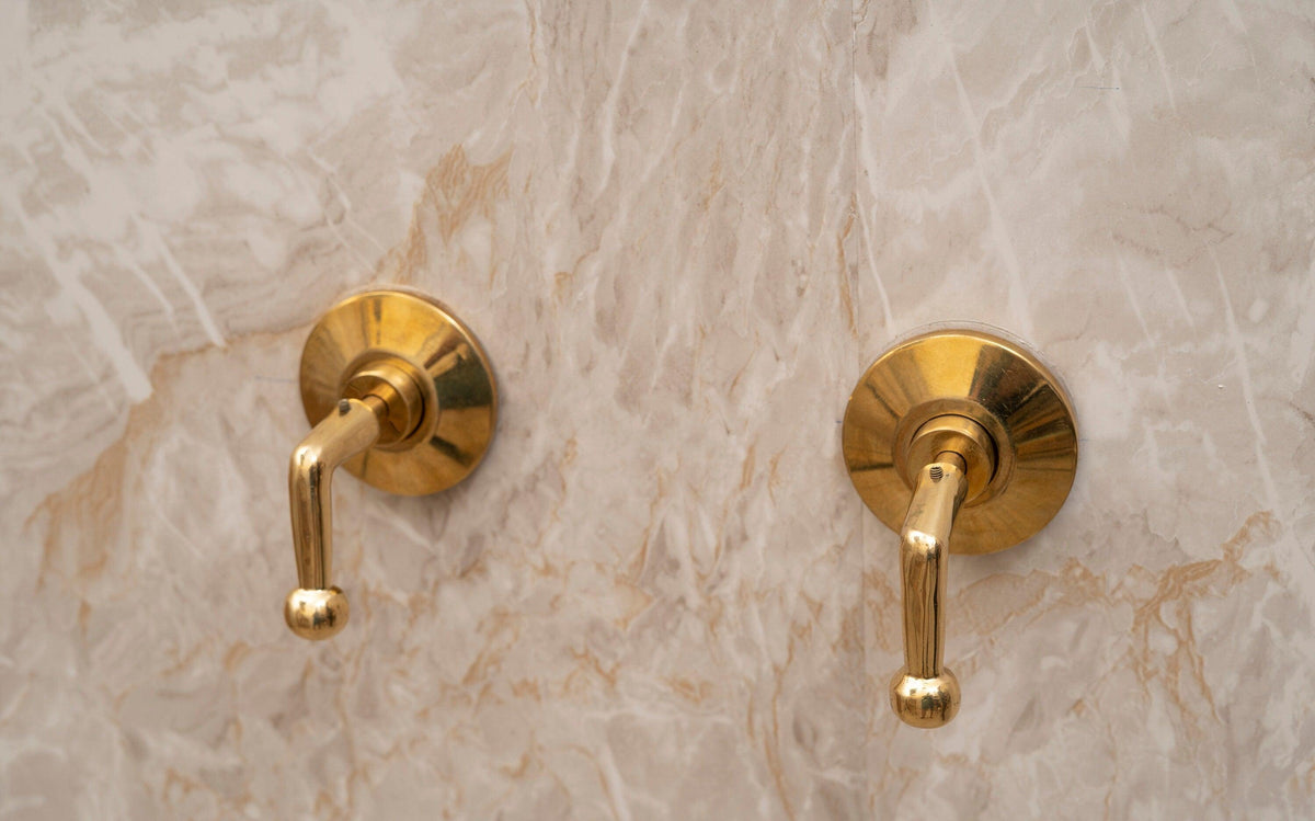 Pair of unlacquered brass shower lever handles with round trim plates installed on marble