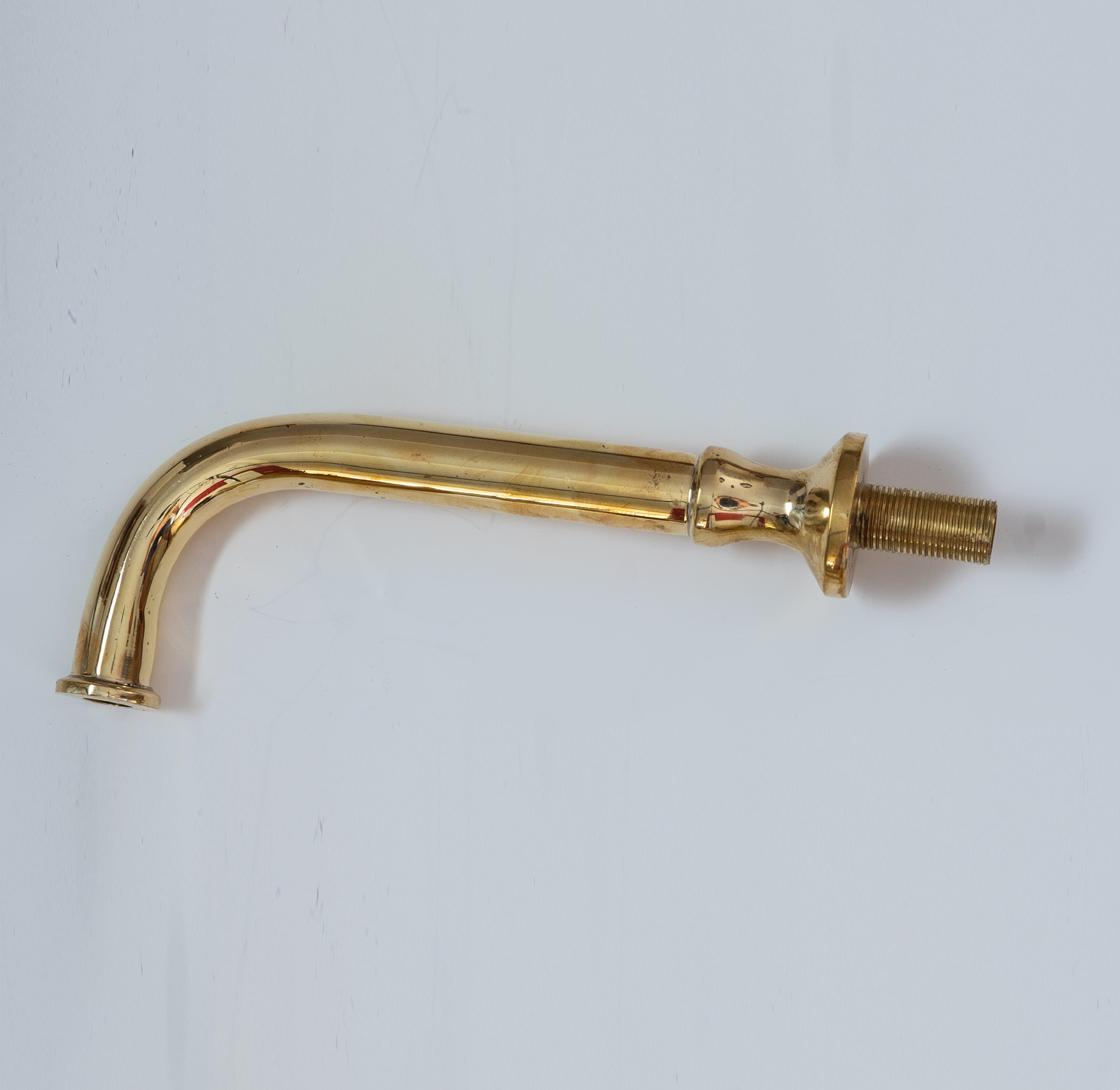 Close-up of an unlacquered brass curved spout for a wall-mounted bathroom faucet