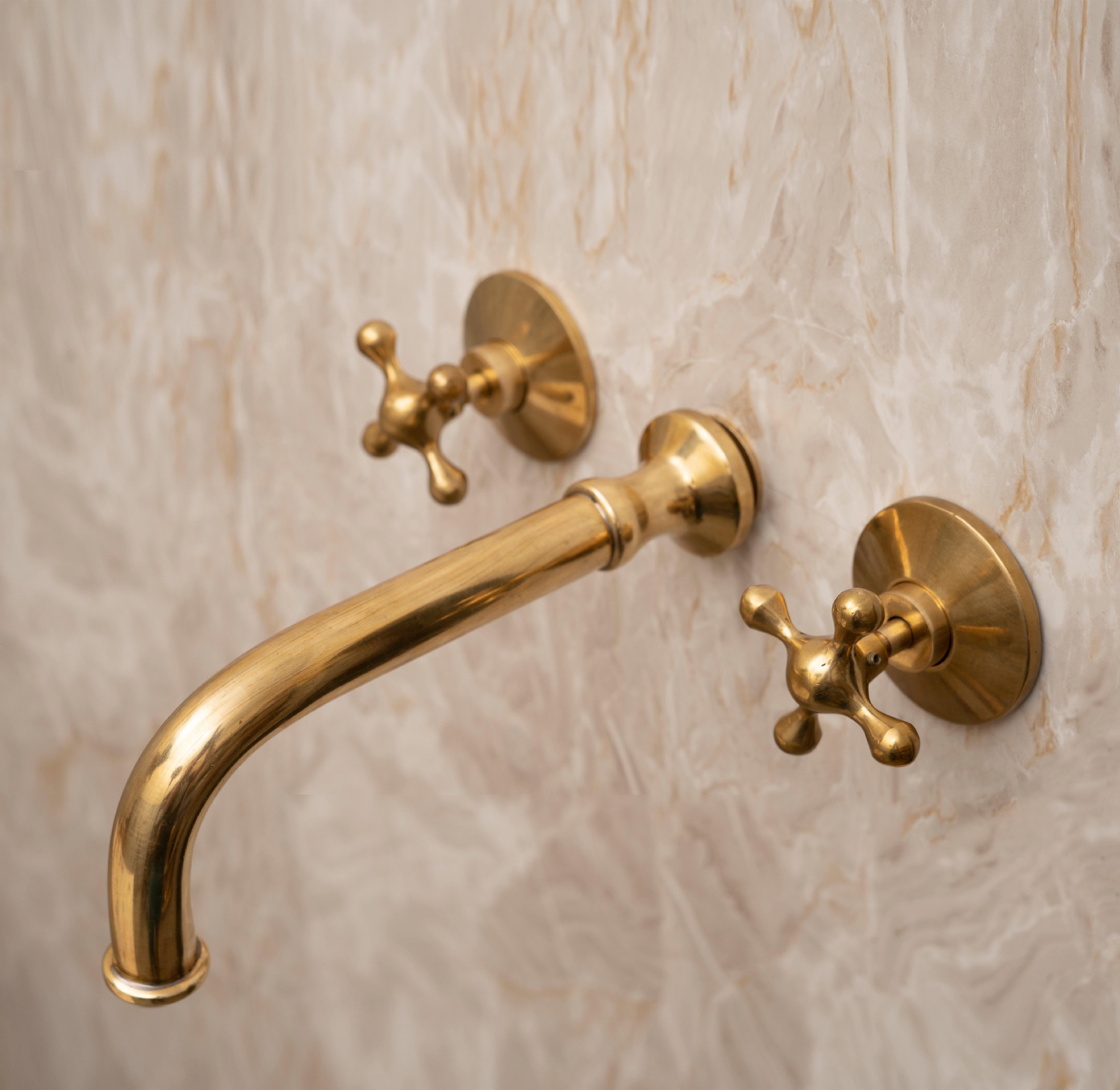 Angled view of an unlacquered brass wall-mounted bathroom faucet with cross handles