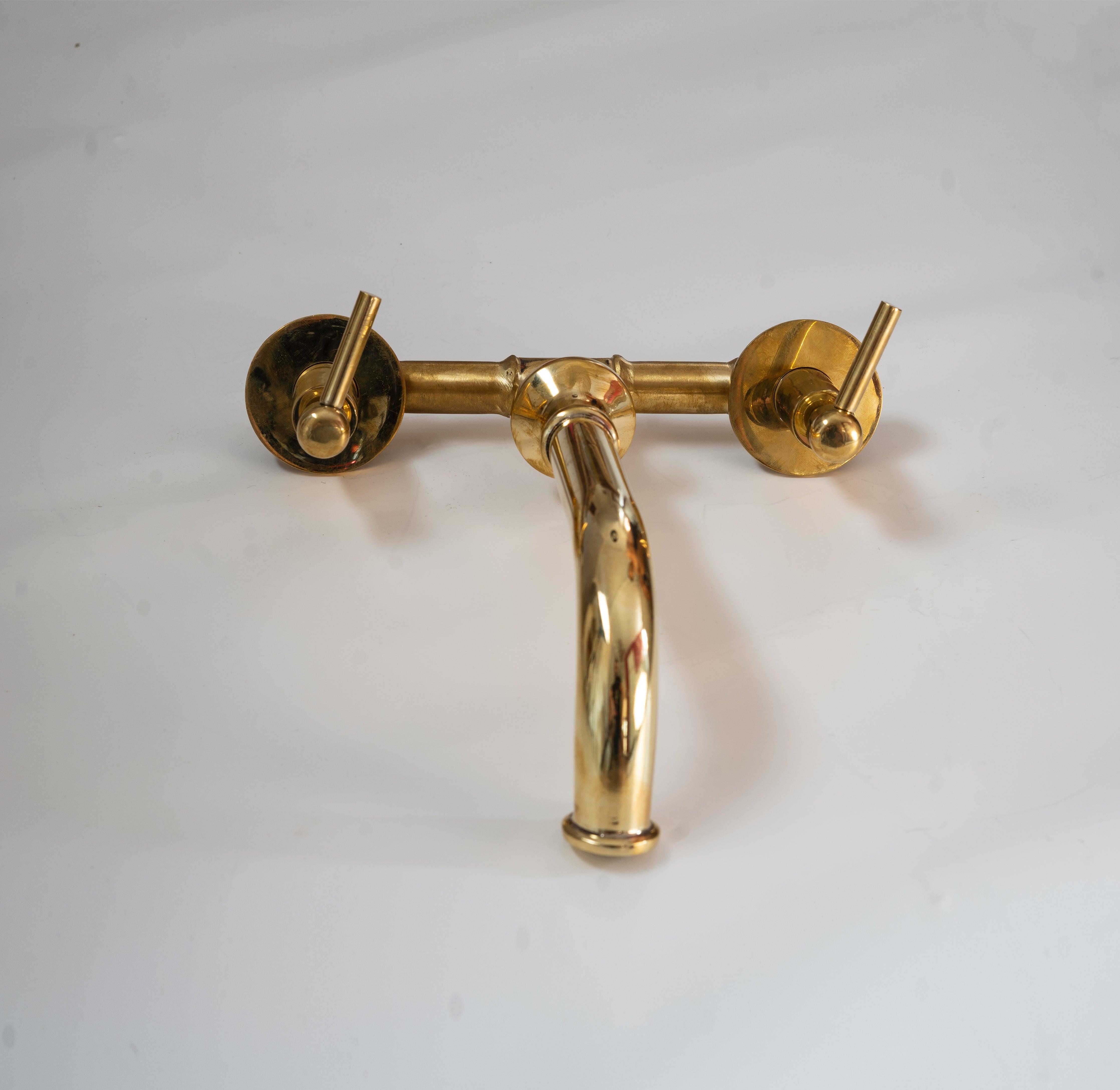 Front view of an unlacquered brass wall-mounted sink faucet with lever handles
