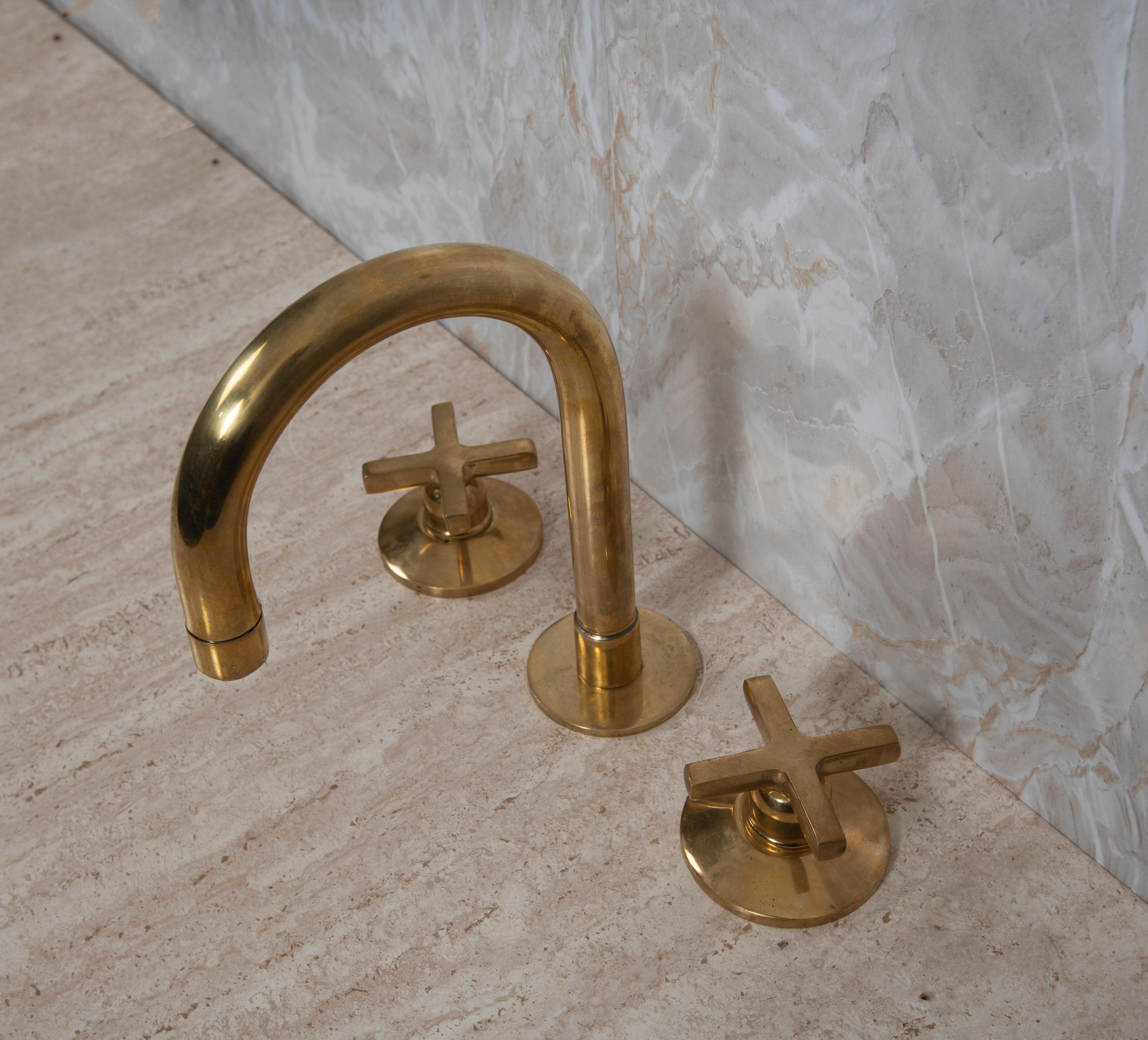 Unlacquered brass widespread bathroom faucet with cross handles installed on marble