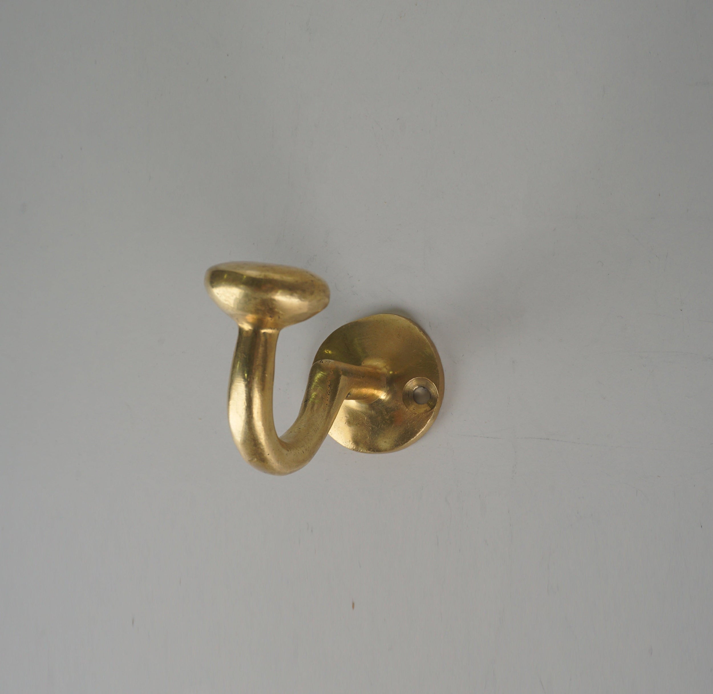 Side view of a vintage solid brass single wall coat hook with round mounting plate
