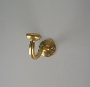 Side view of a vintage solid brass single wall coat hook with round mounting plate