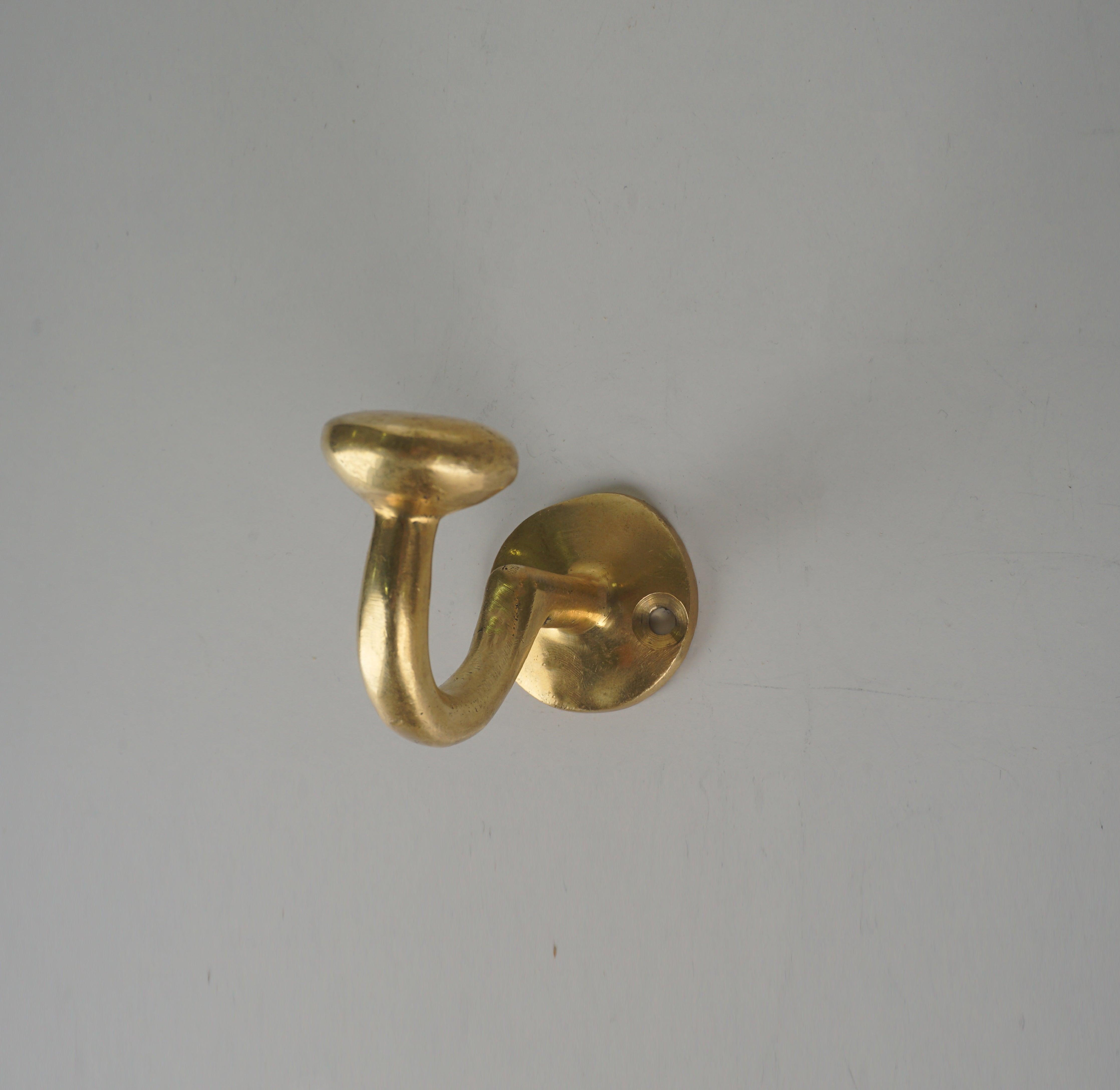 Side view of a vintage solid brass single wall coat hook with round mounting plate