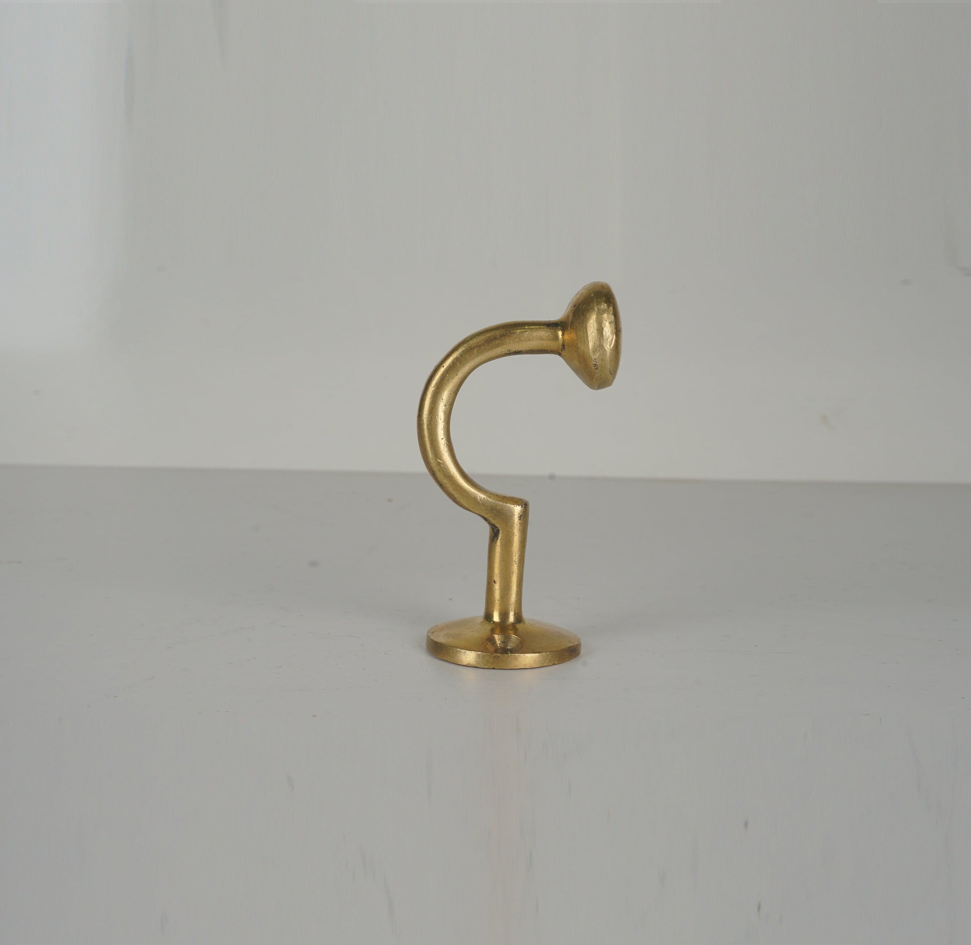 Profile view of a vintage unlacquered brass wall hook with curved stem
