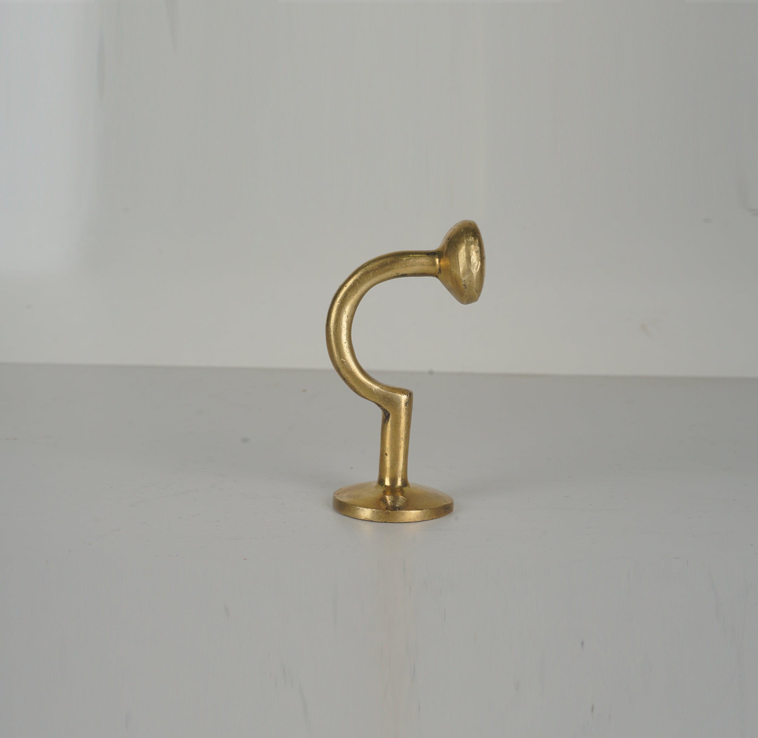 Profile view of a vintage unlacquered brass wall hook with curved stem